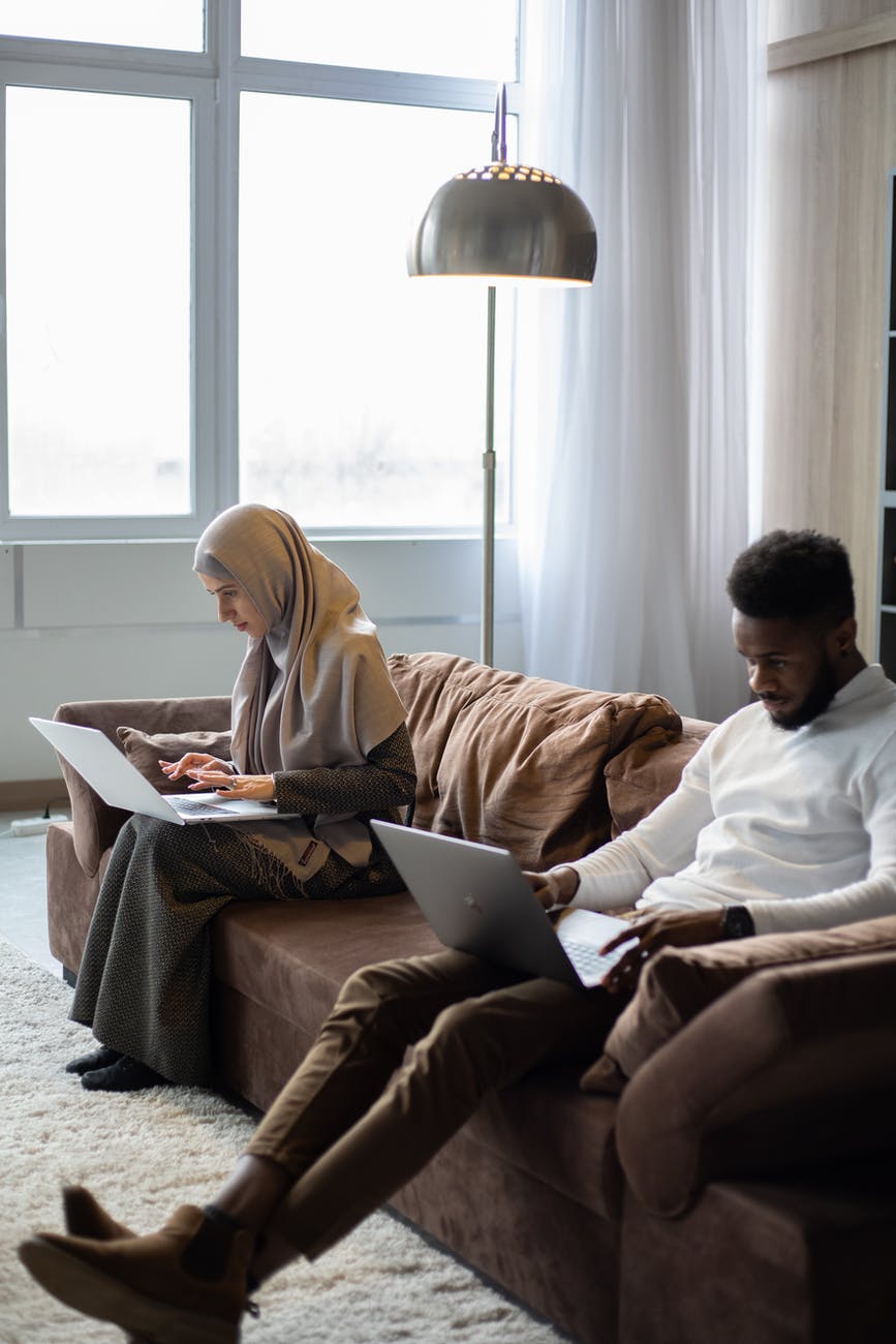 multiethnic couple of freelancers working on laptops on sofa at home