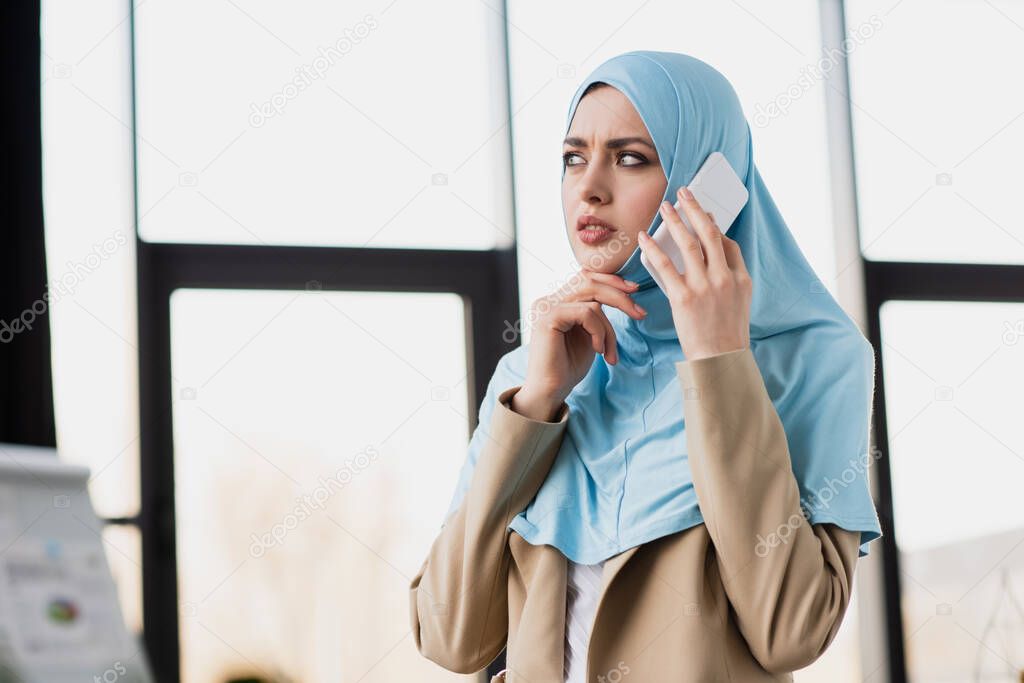 thoughtful arabian businesswoman in hijab talking on cellphone in office