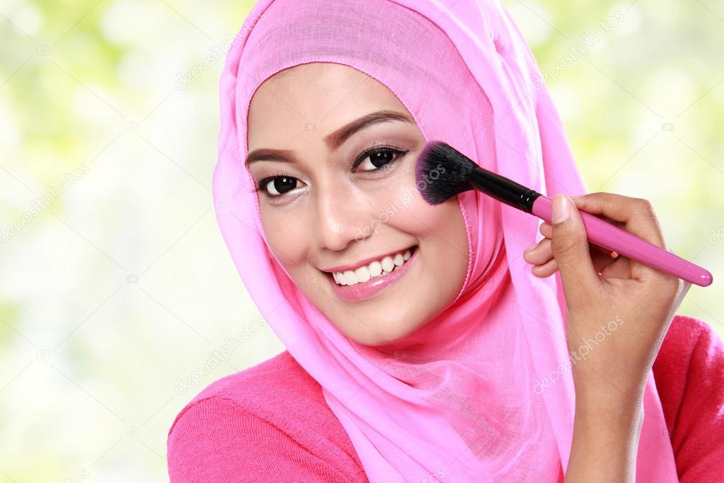 young muslim woman applying blush on