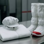 Peralatan pakaian ruang bersih tersusun rapi di atas meja stainless steel, menampilkan kebersihan pakaian ruang bersih dengan bahan non-shedding dan higienis beraksen merah lembut.