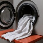 Mesin laundry industri sedang mencuci seragam ESD konduktif berwarna putih, menampilkan detail bahan antistatik dengan aksen merah yang lembut, menggambarkan pentingnya proses laundry seragam ESD konduktif.